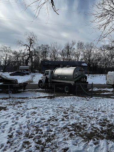 A vacuum truck is parked in the snow in front of a house.