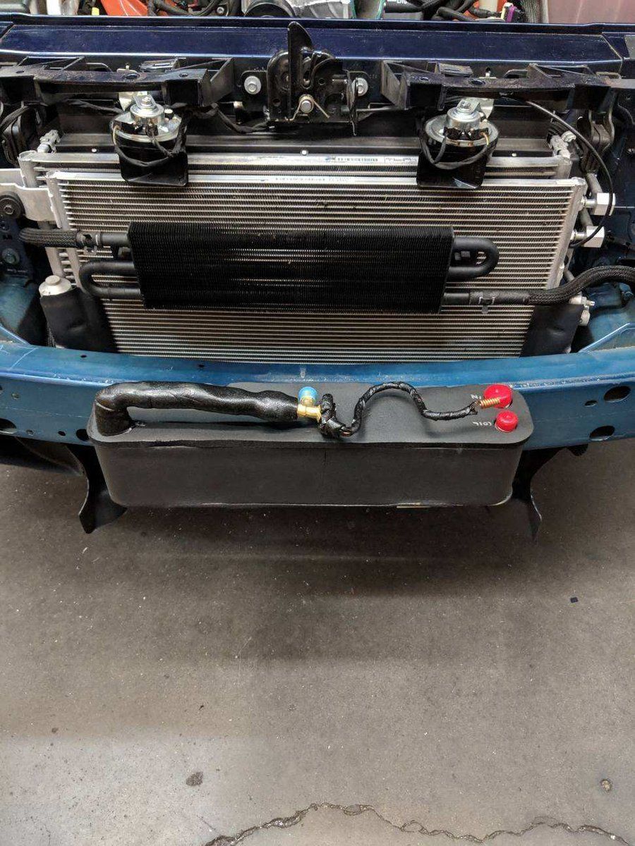 Front view of a blue car with the grille removed, showing the radiator and front-mounted oil cooler.
