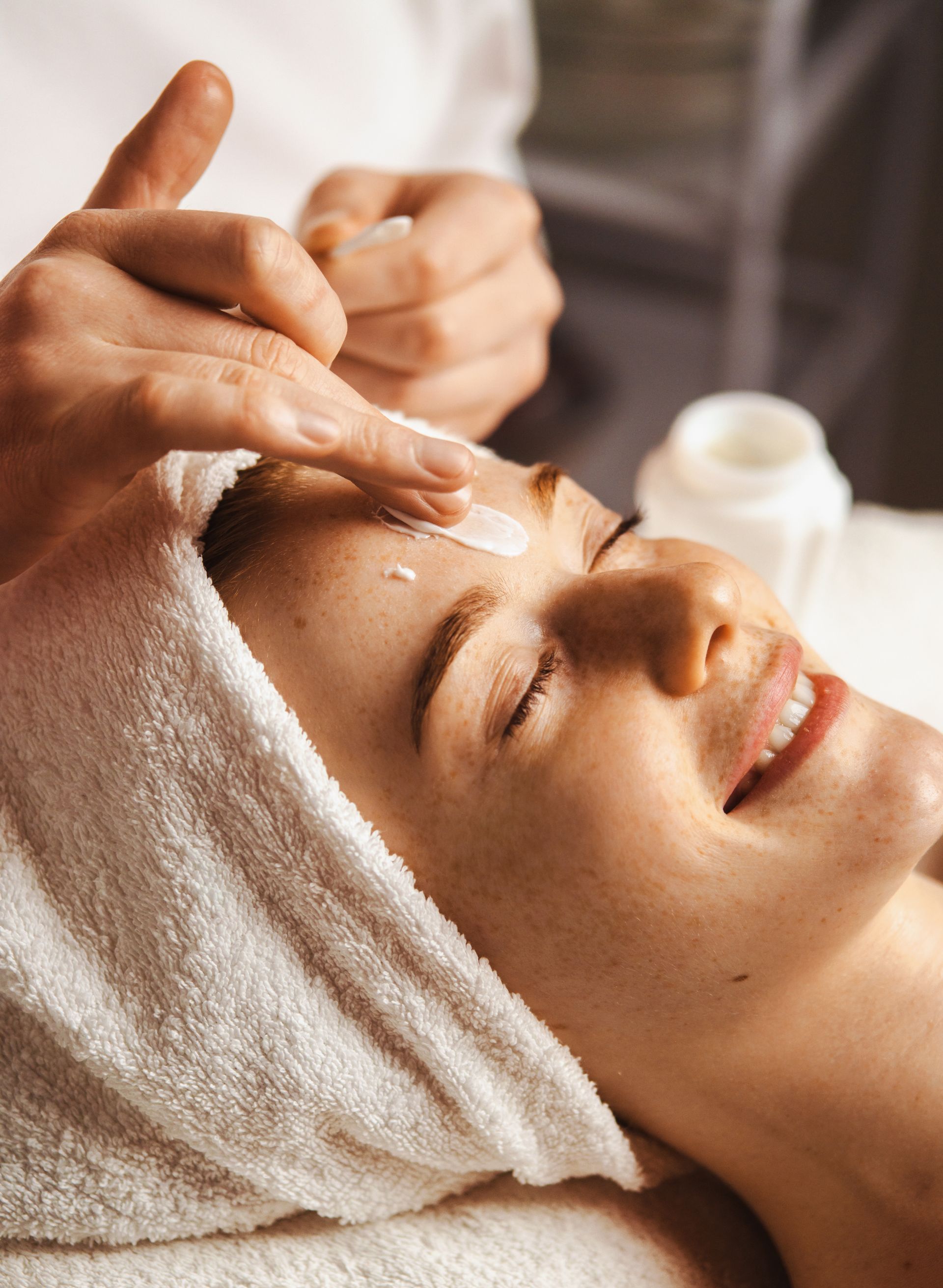 Eine Frau mit einem Handtuch um den Kopf bekommt in einem Spa eine Gesichtsbehandlung.