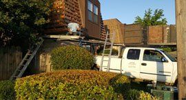 roofing crew with truck and ladders at house with a steep roof