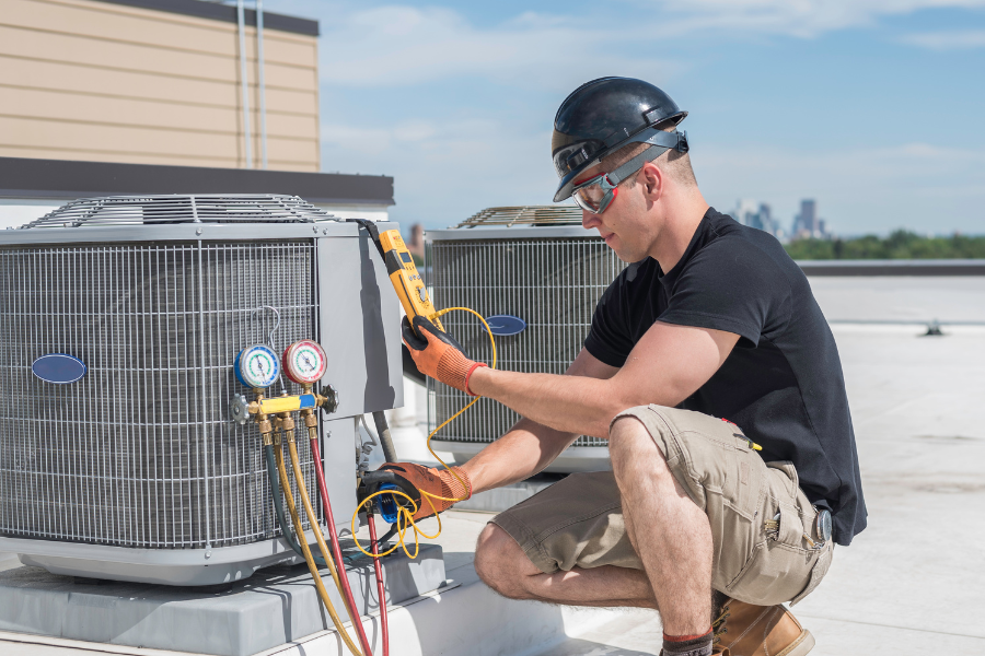 A man is working on an air conditioner on the roof of a building.