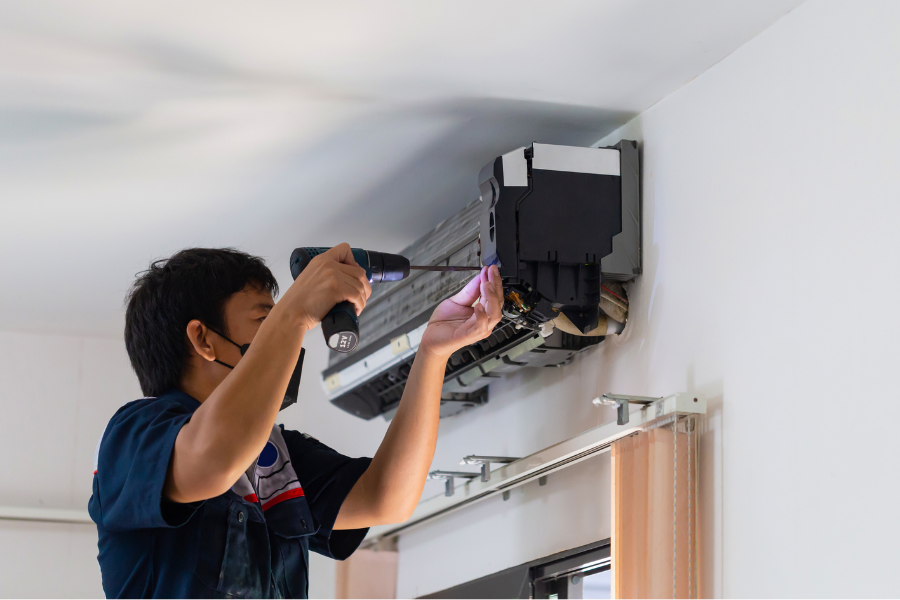 A man is fixing an air conditioner with a screwdriver.