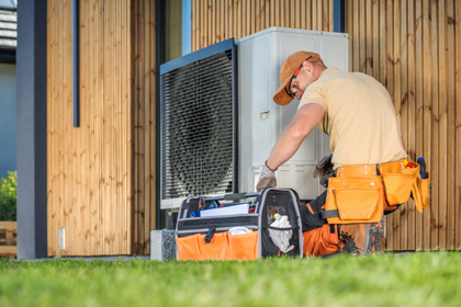 A man is working on a heat pump outside of a house.