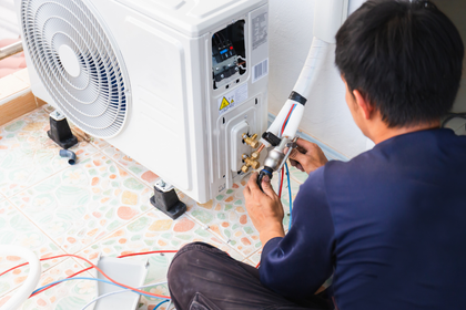 A man is sitting on the floor fixing an air conditioner.