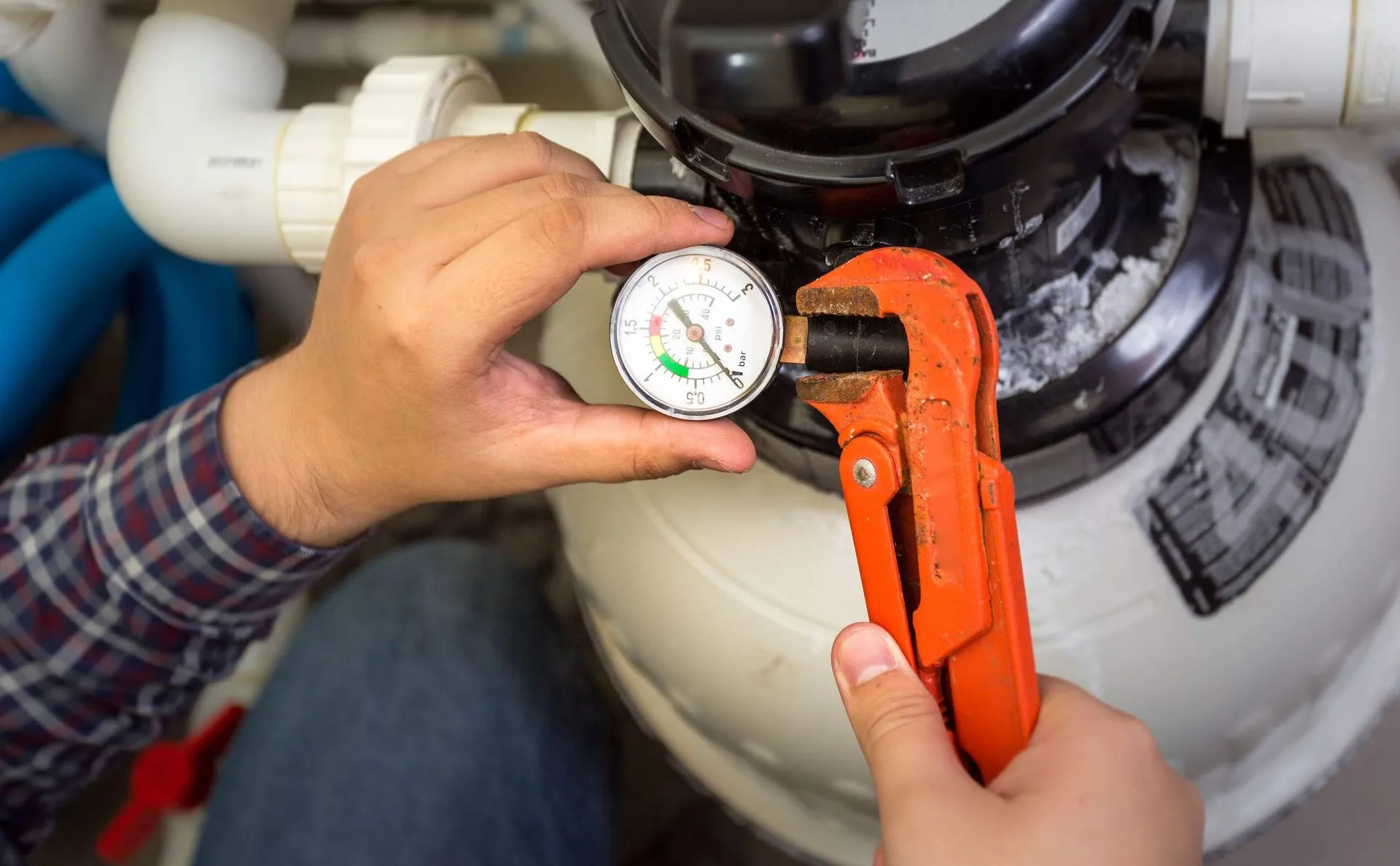 A man is fixing a pool filter with a wrench and a pressure gauge.