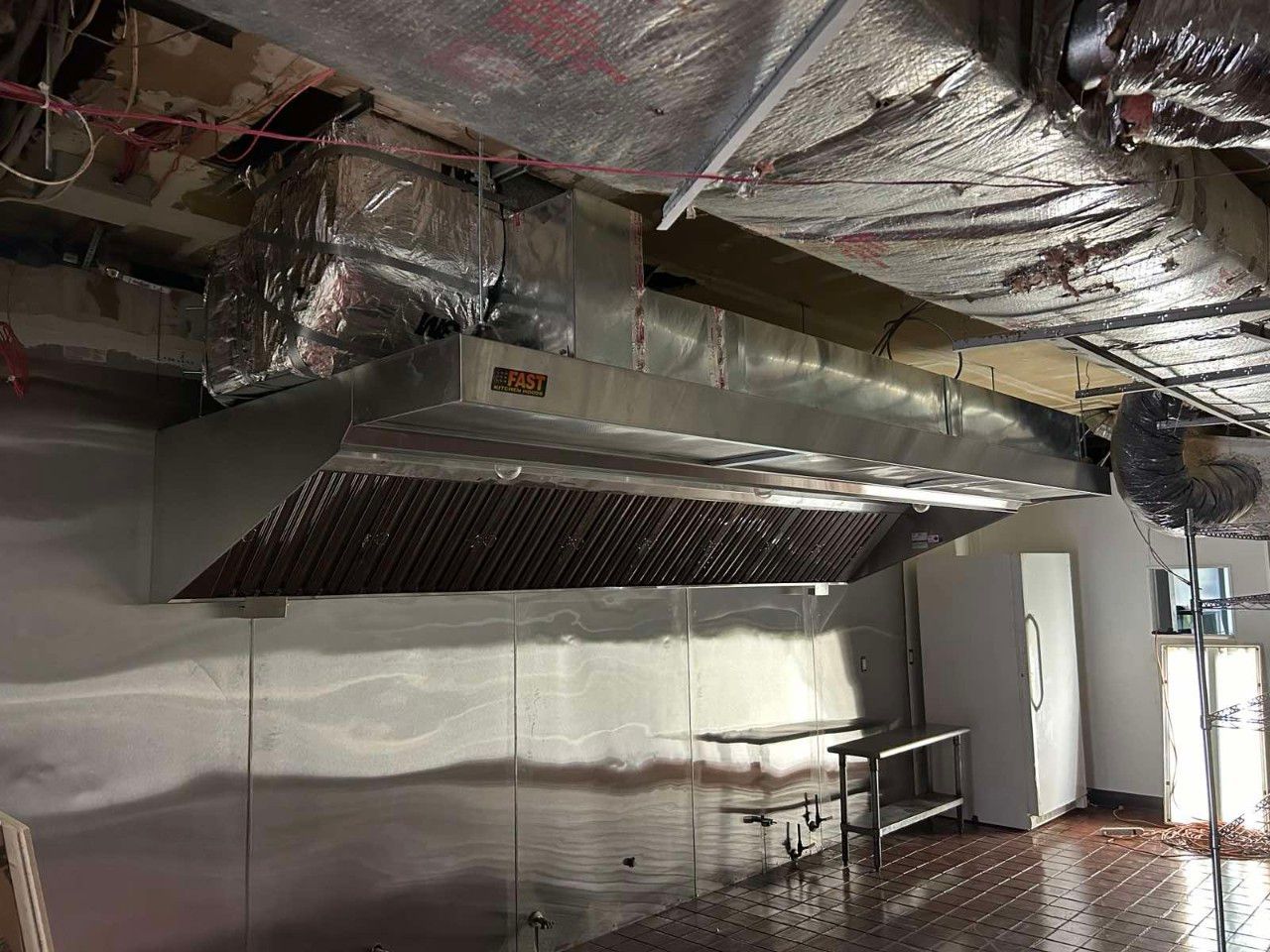 A kitchen with a stainless steel hood hanging from the ceiling.