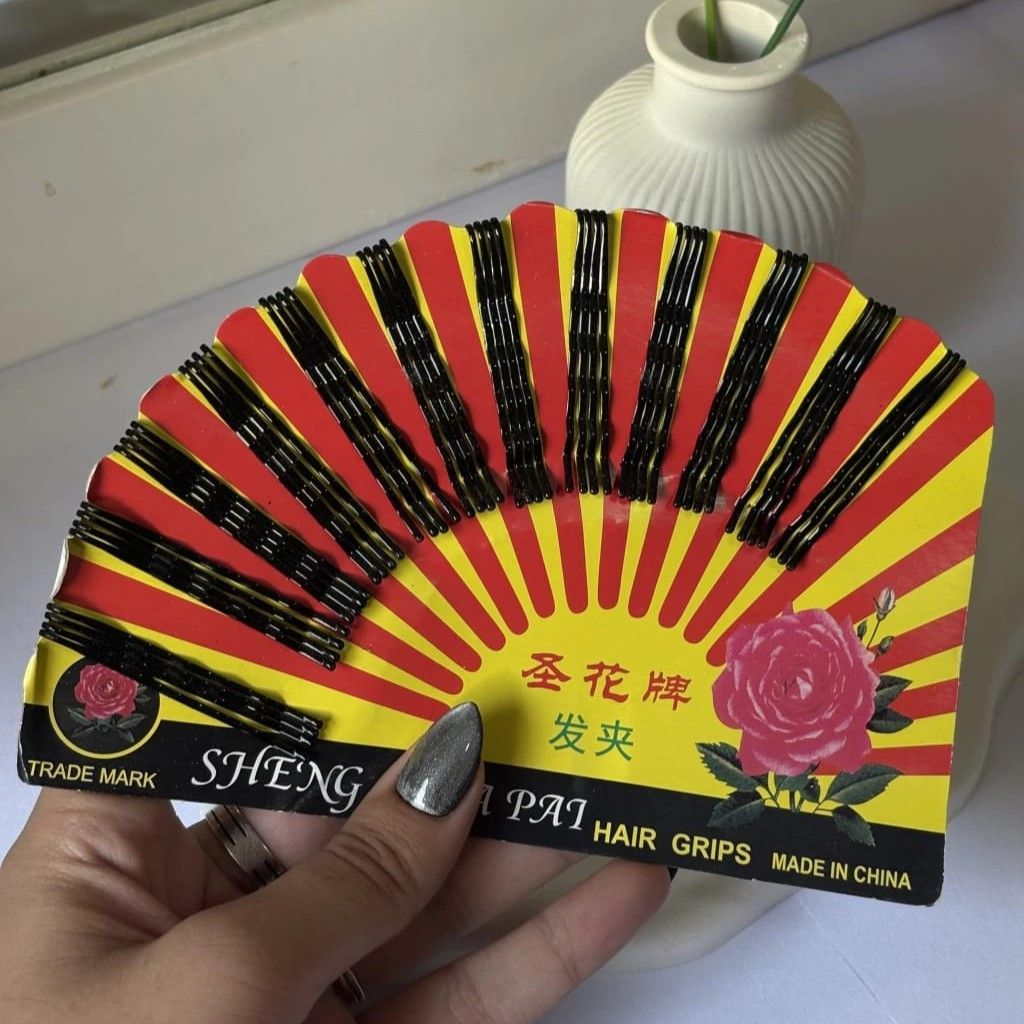 Mano sosteniendo un paquete de horquillas para el cabello negras sobre una tarjeta con diseño de rayos.