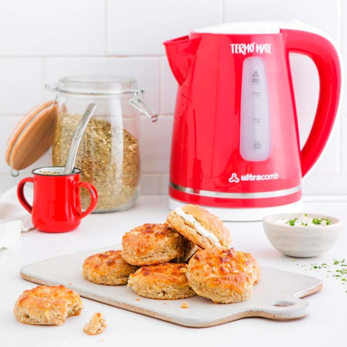Hervidor eléctrico rojo, galletas y una taza de té sobre una encimera blanca.