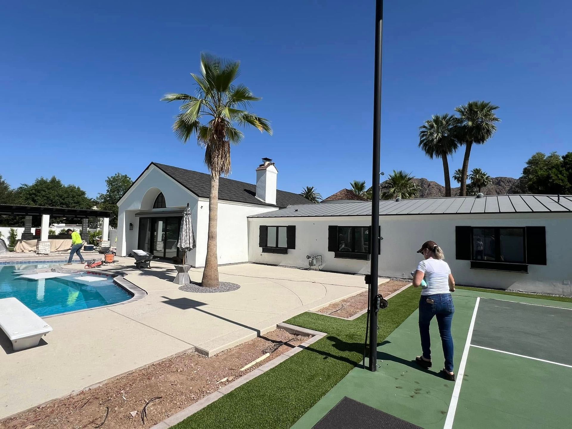 A woman is standing on a tennis court in front of a house with a pool