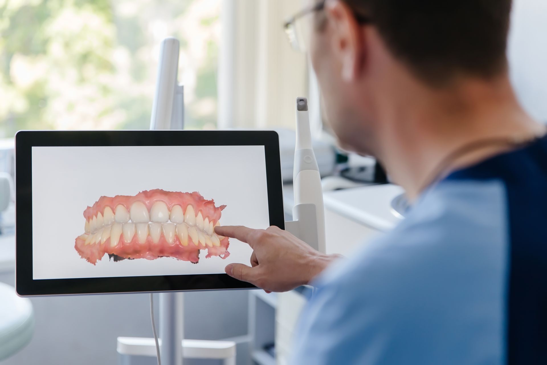 A dentist is looking imaging teeth on a tablet.