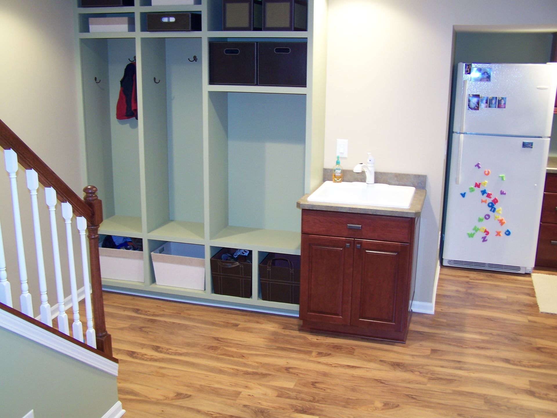 Entryway with custom lockers, a utility sink, and refrigerator. Wood flooring.