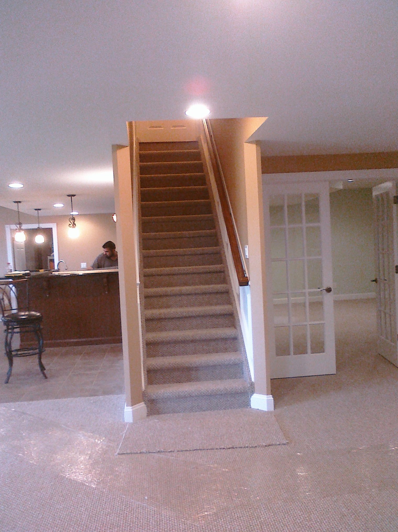Staircase with brown carpet leads up from a basement with a bar area and French doors.