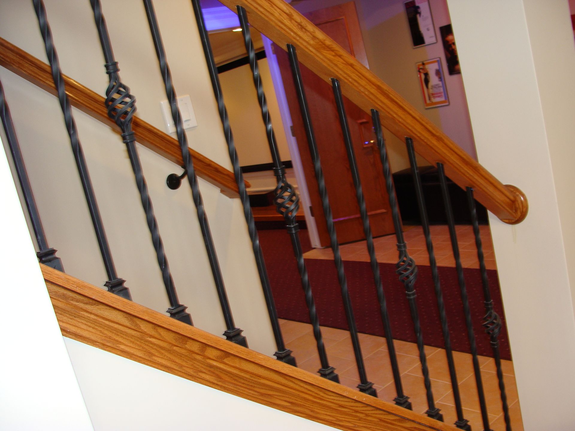 Wooden staircase with black iron spindles, brown handrail, and beige walls.
