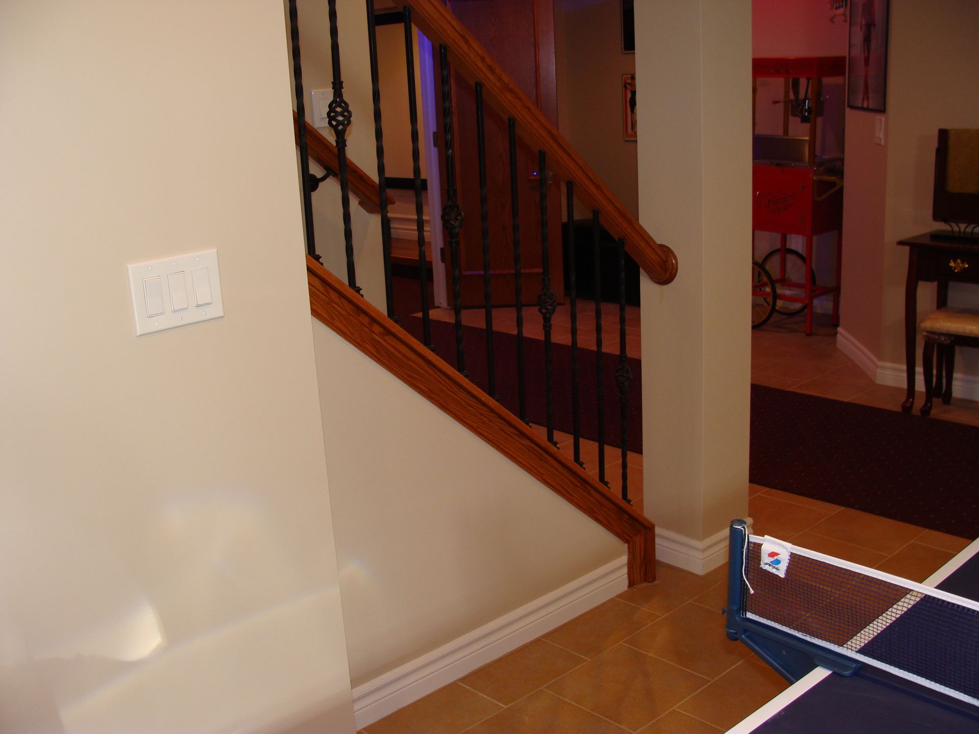 Staircase with wooden banister and black metal spindles, leading down to a room with a popcorn machine.
