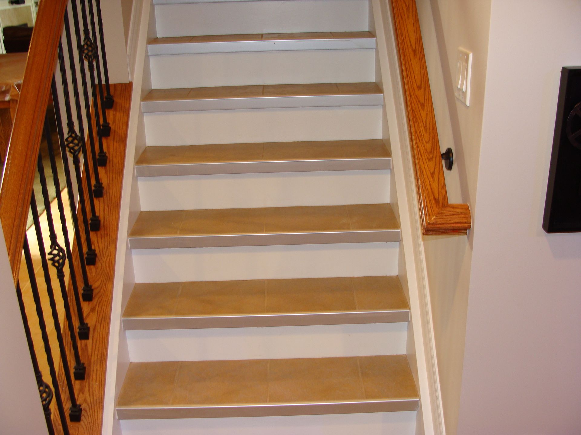 Staircase with wooden steps, white risers, and a wooden handrail on the right and black iron railing on the left.