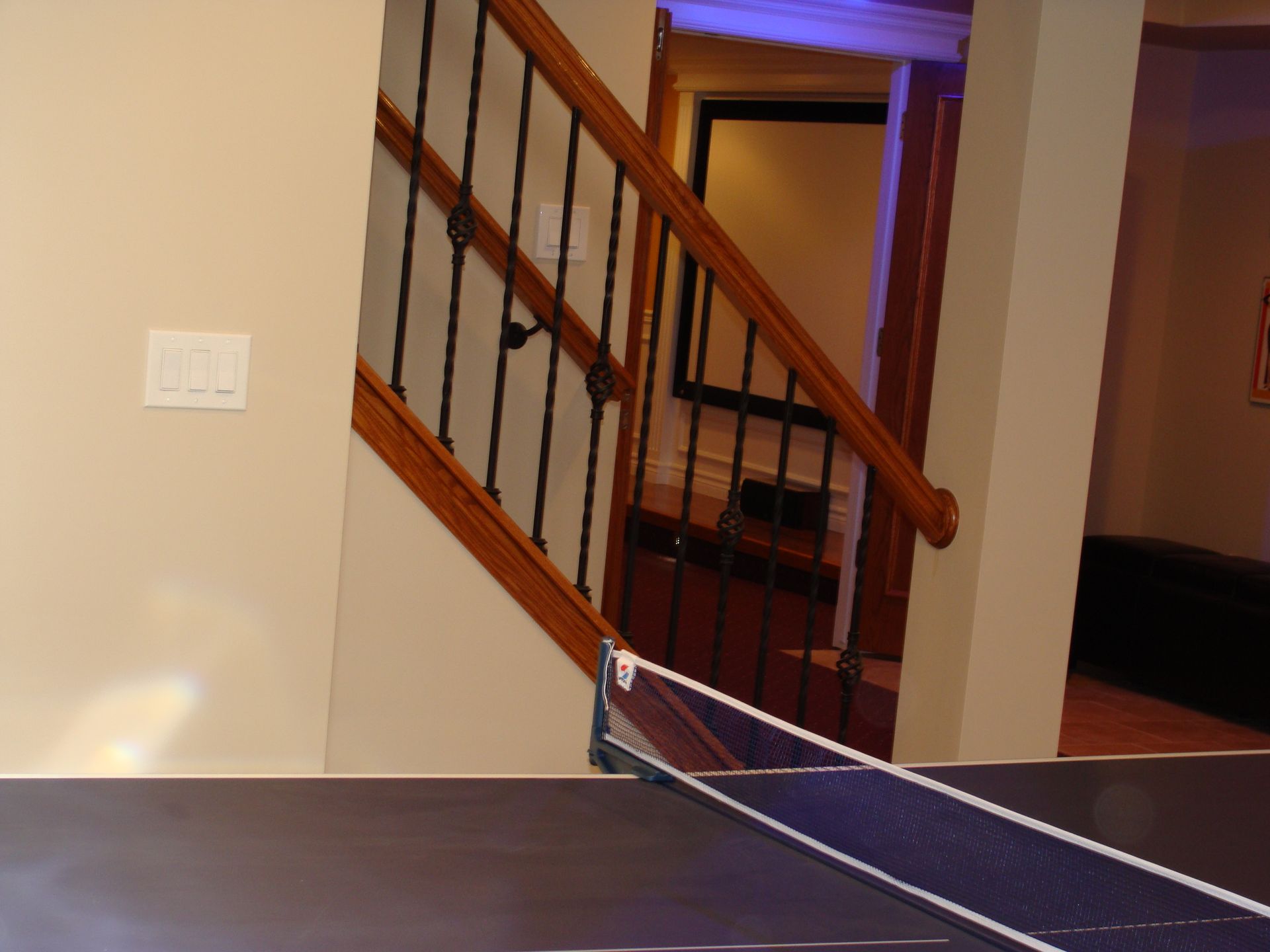 Ping pong table net, stairs, and door frame in a beige-walled basement.