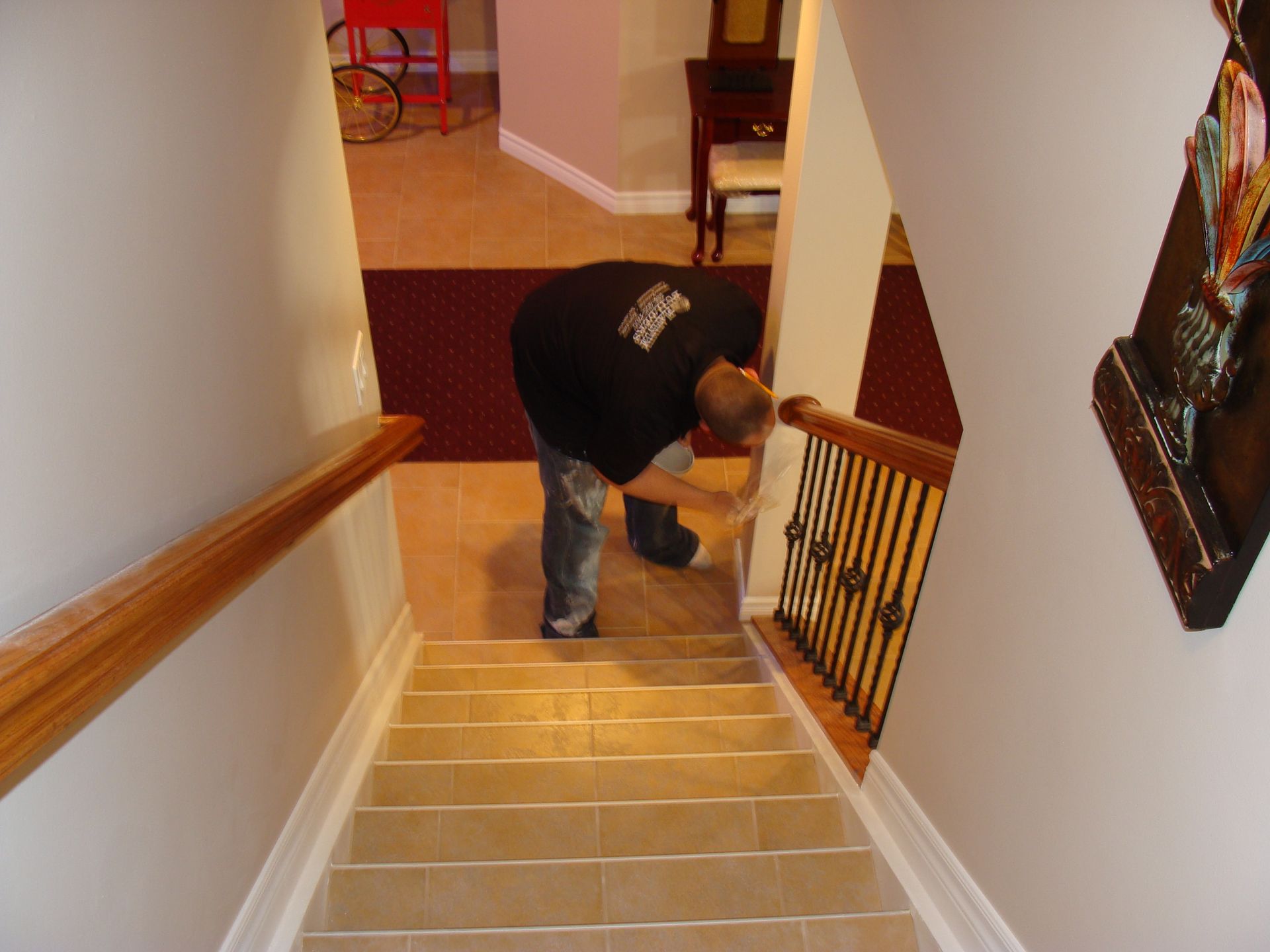 Man inspecting the end of a stair railing.  Beige tiled stairs, light walls, red carpet in background.