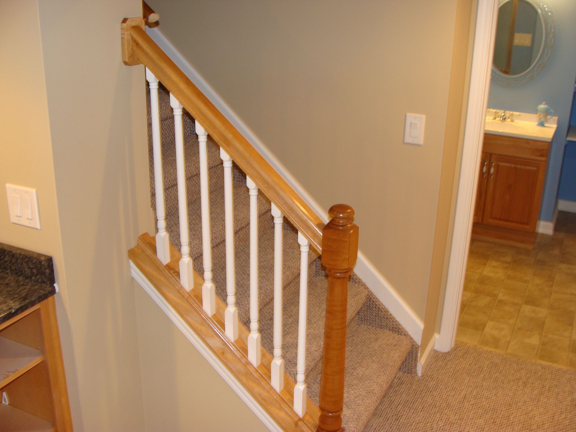 Staircase with wooden railing and white spindles, leading to a bathroom with a vanity.