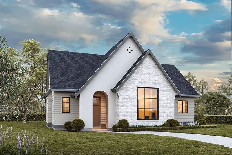 Cottage-style house with white brick and gray roof, arched entry, large front window, and manicured lawn under a cloudy sky.