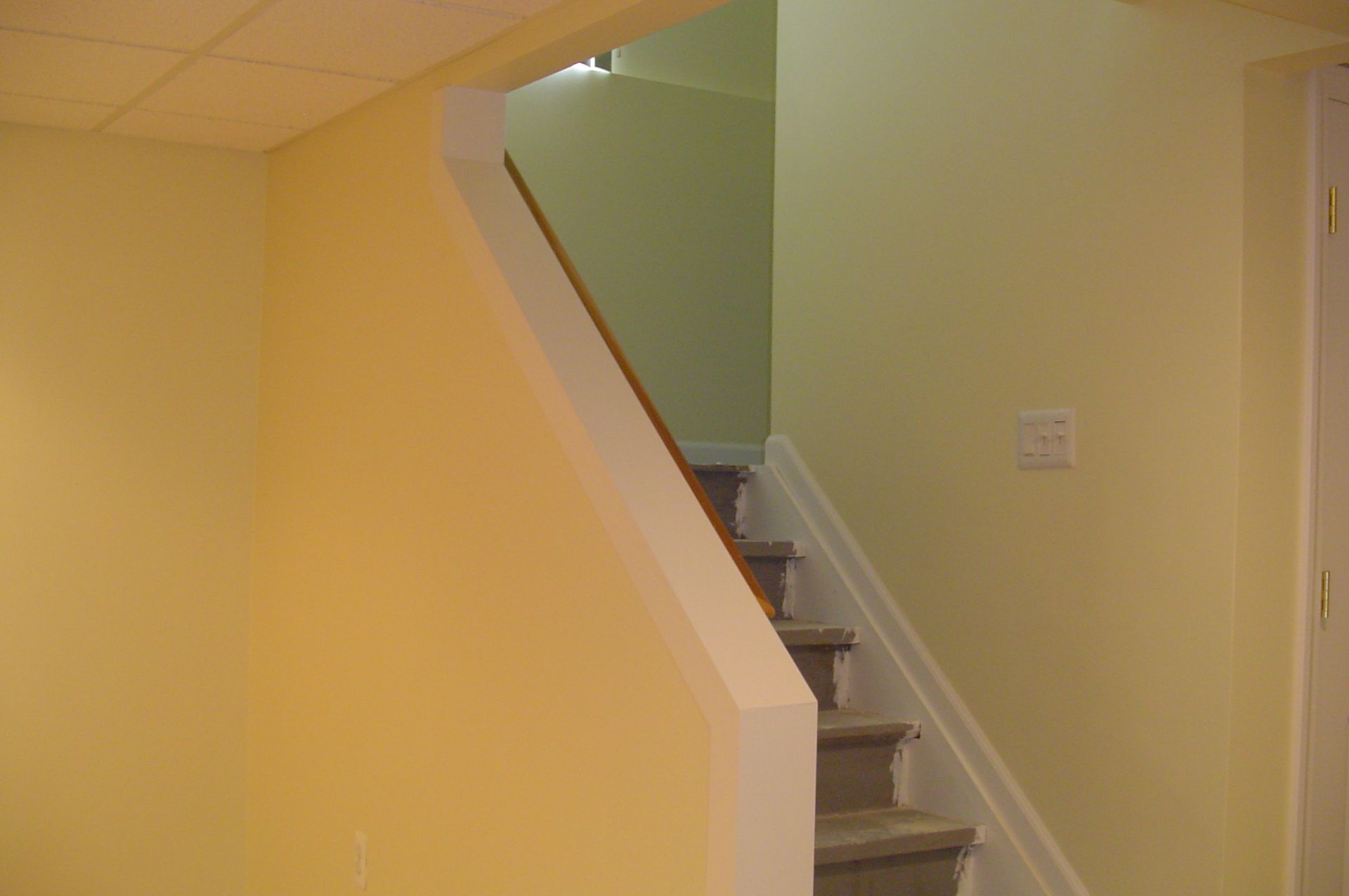 Staircase with yellow and light green walls, leading upwards. White railing and trim.