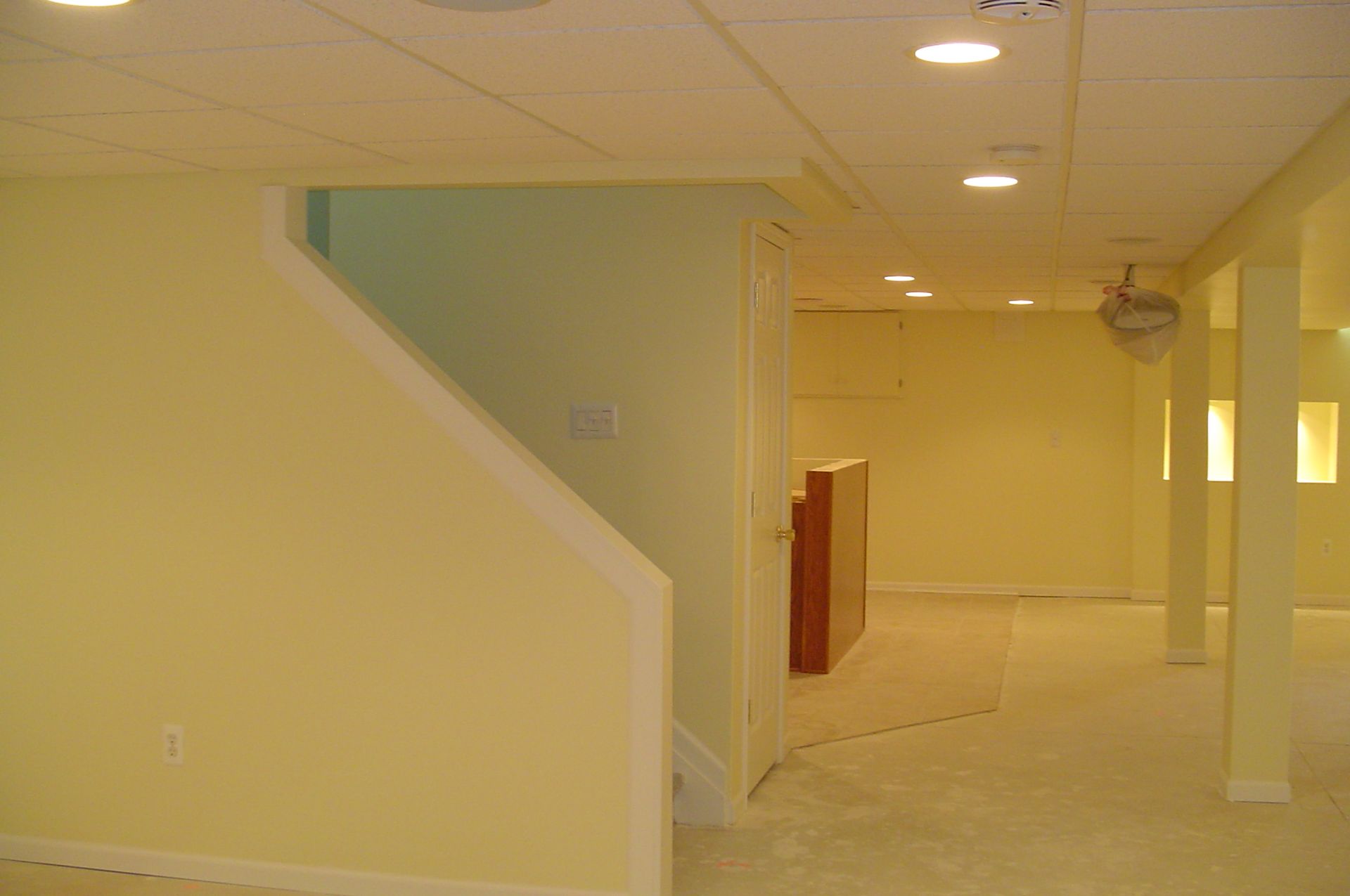 Yellow-painted basement with staircase on left, recessed lighting, and open space.