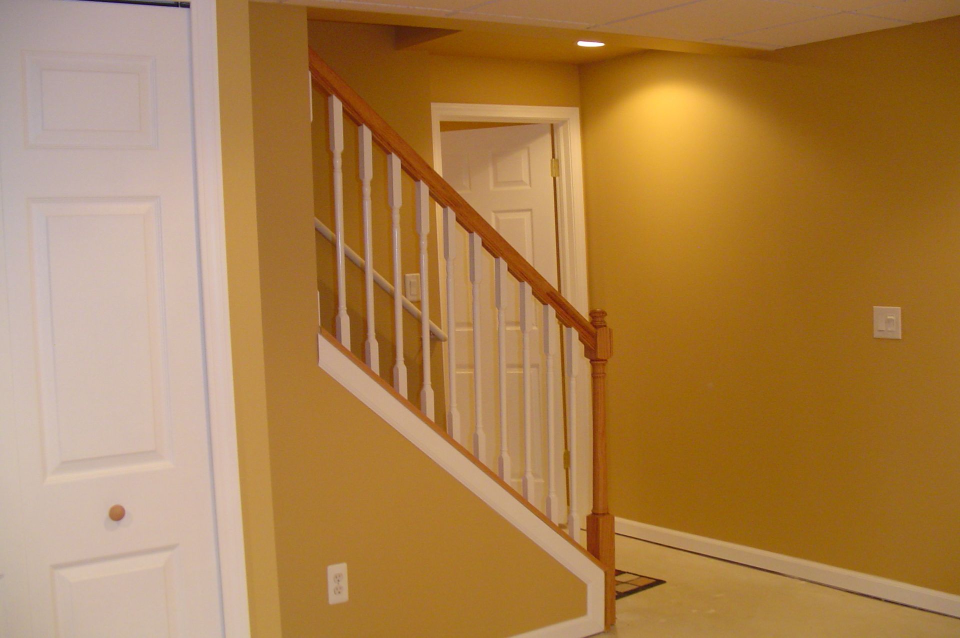 Staircase with white railings and wooden handrail in a room with golden yellow walls and a white door.
