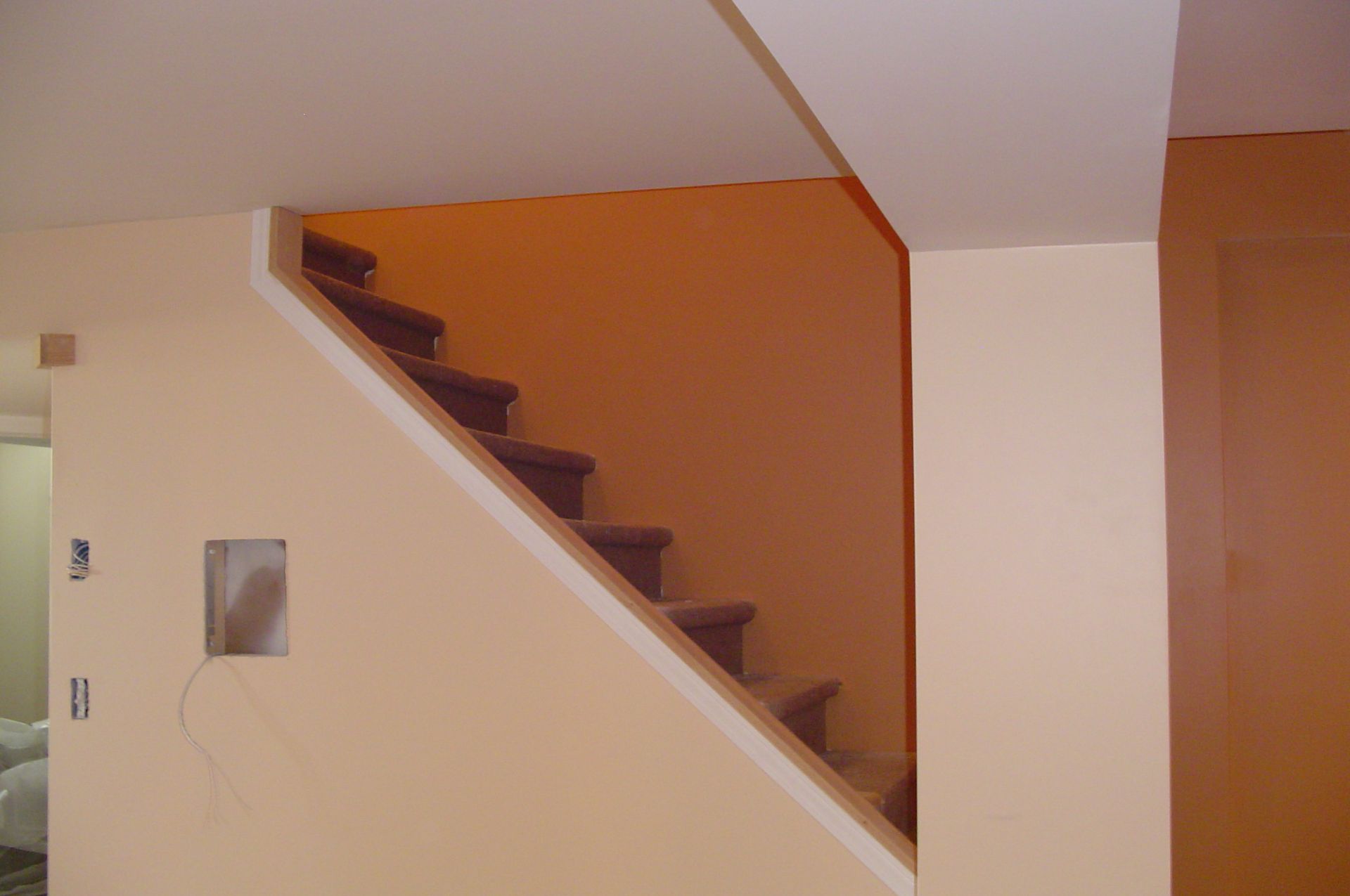 Staircase painted beige, ascending to a recessed area; bare wiring and electrical box visible on wall.