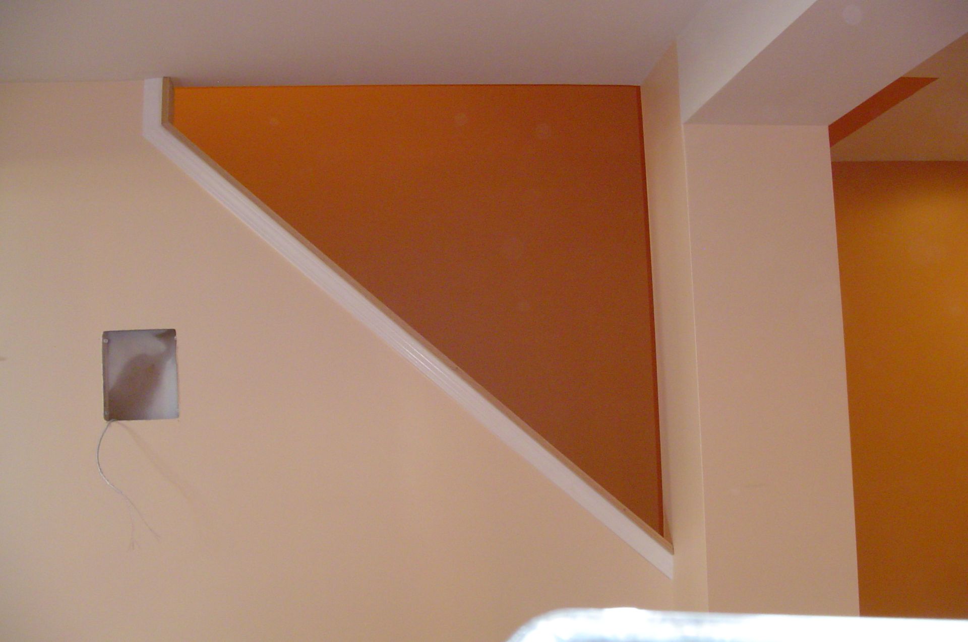 Orange triangle shape on tan wall with white trim.