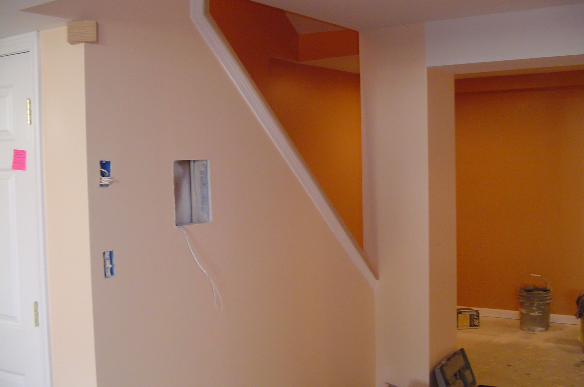 Interior view of a stairwell painted peach with a white trim. An adjacent room is painted orange.