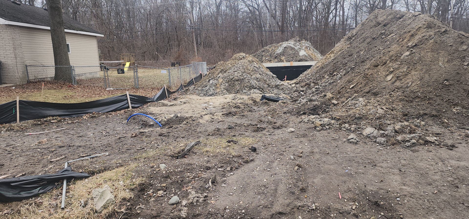 A construction site with dirt piles, a small shelter, and a treeline in the background.