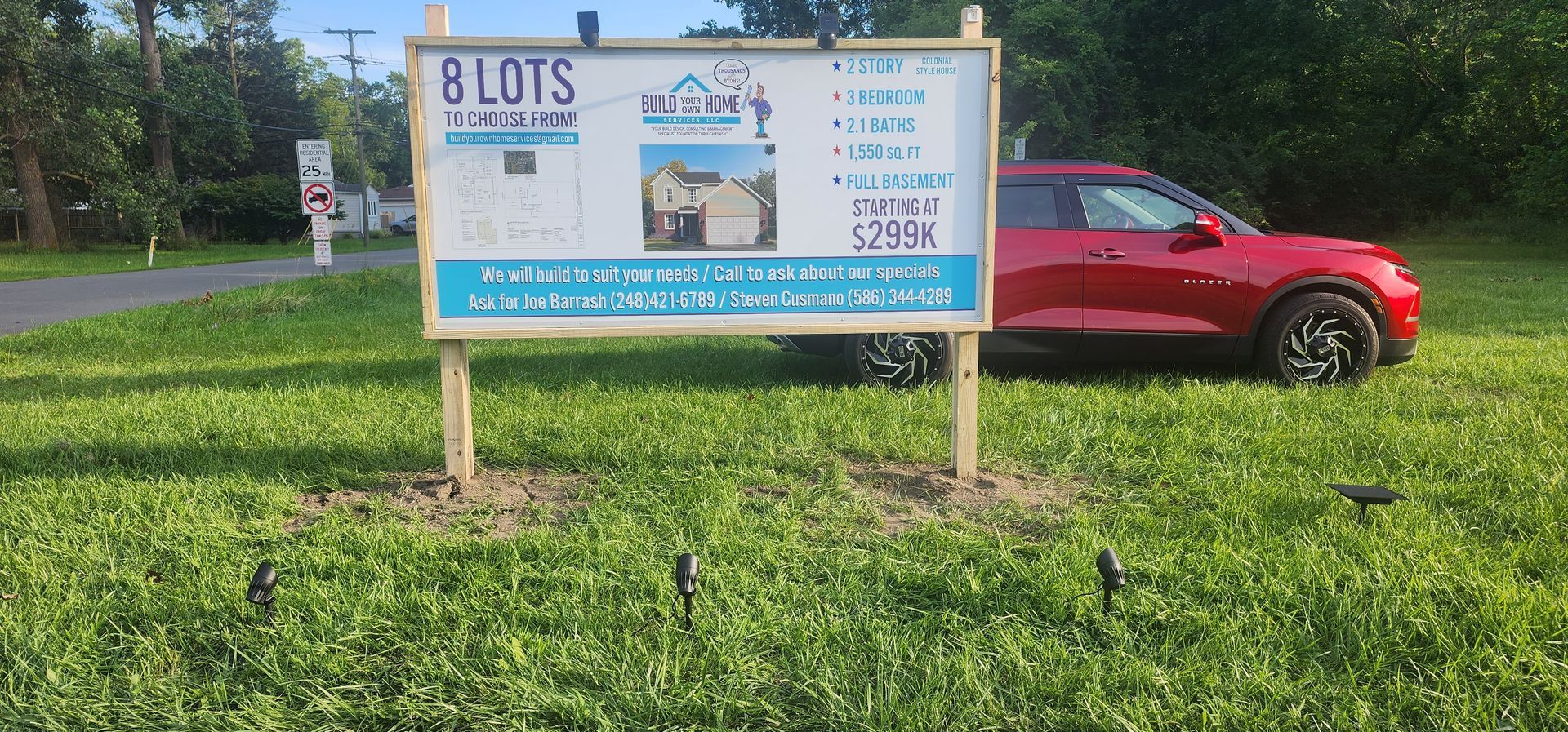 Real estate sign for 8 lots in Woodcreek with a red car parked beside it.