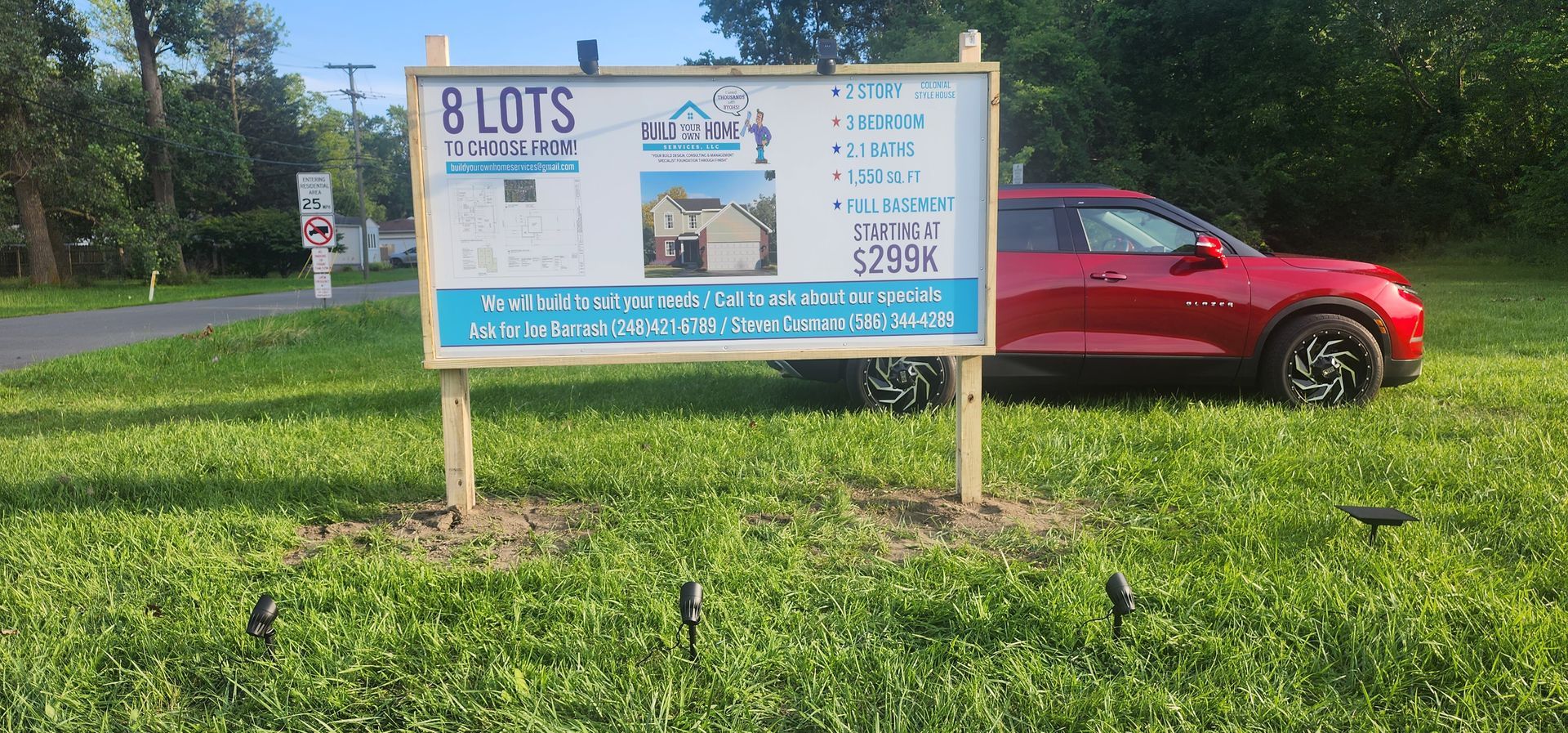 Real estate sign with details of 8 lots for sale, red SUV parked on grass.