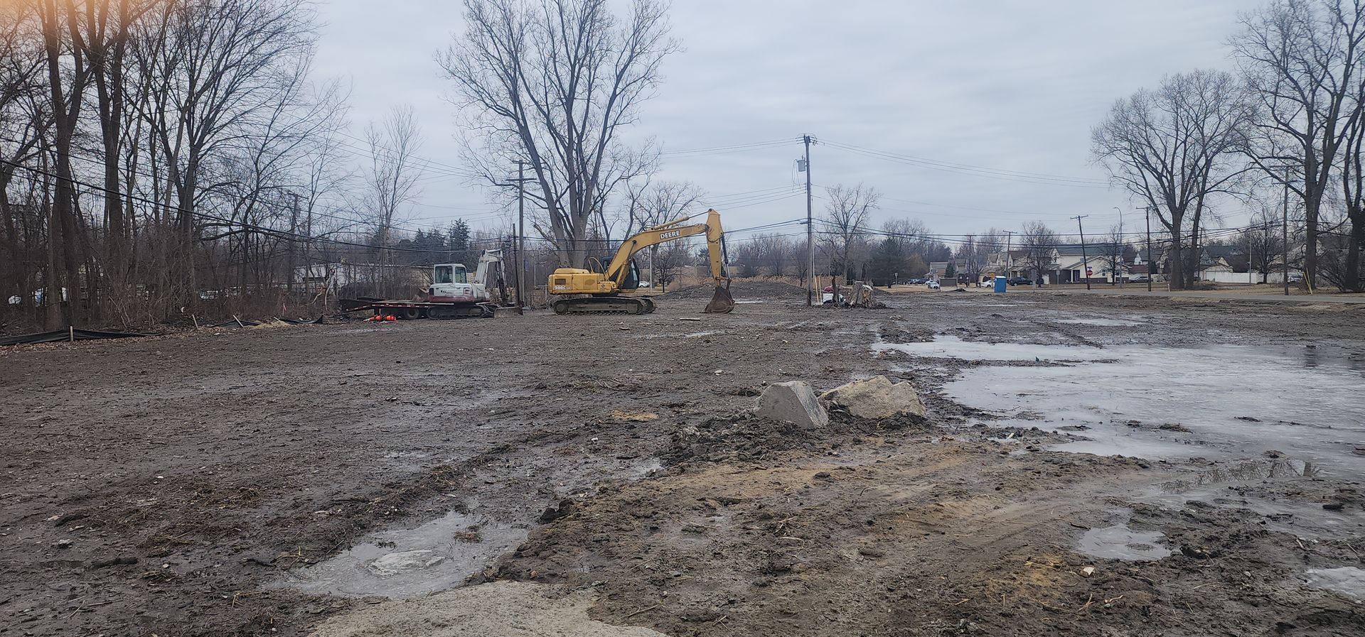 A construction site with heavy machinery and muddy ground under an overcast sky.