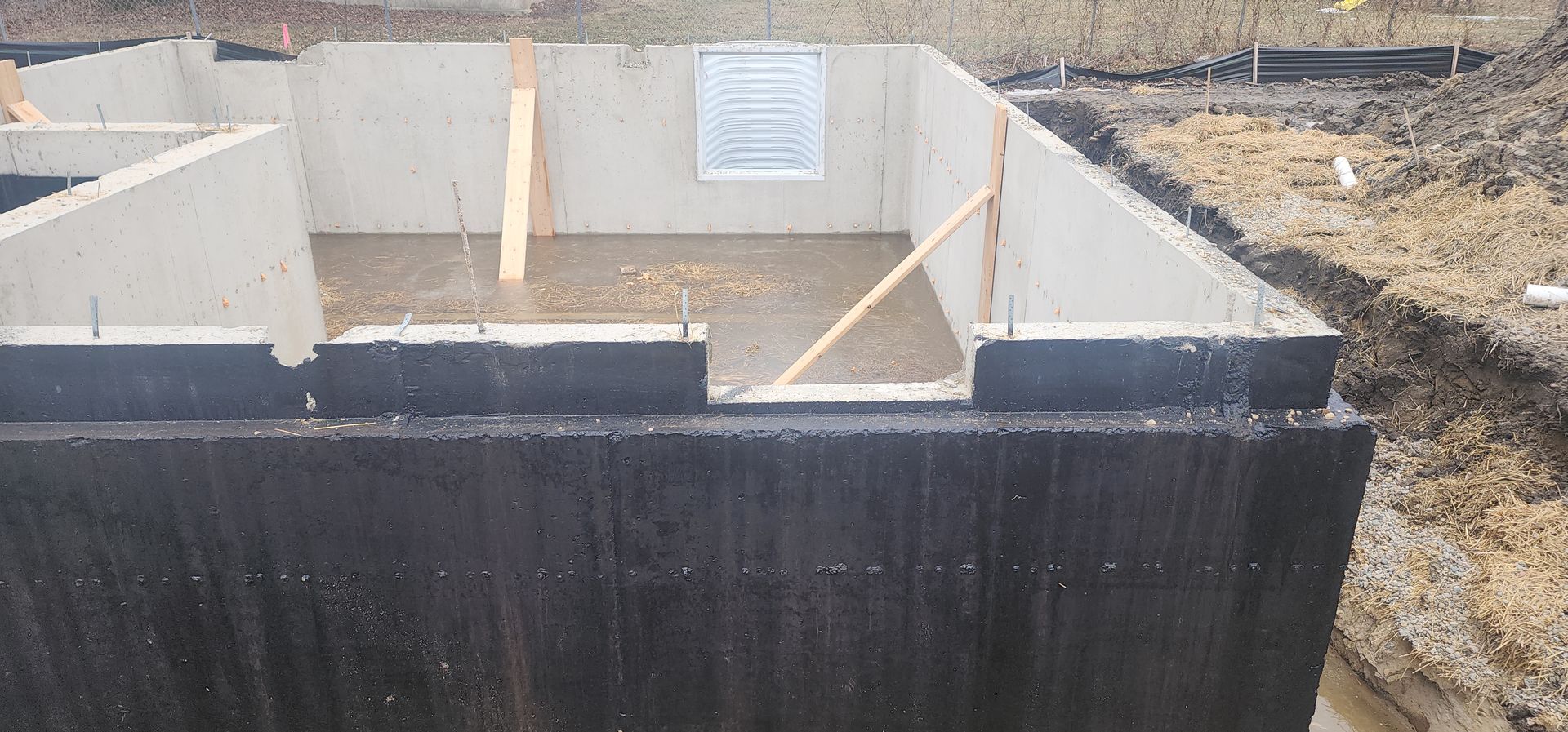 Construction site showing a foundation. Concrete walls are exposed with wooden supports and a window.