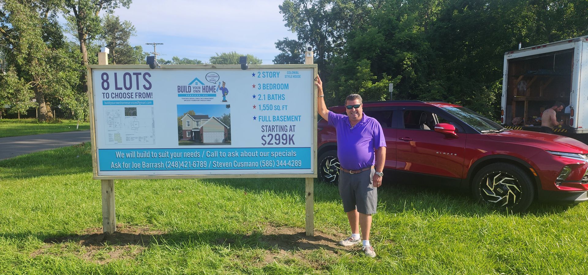 Man standing near a sign for 8 lots, red SUV in the background.