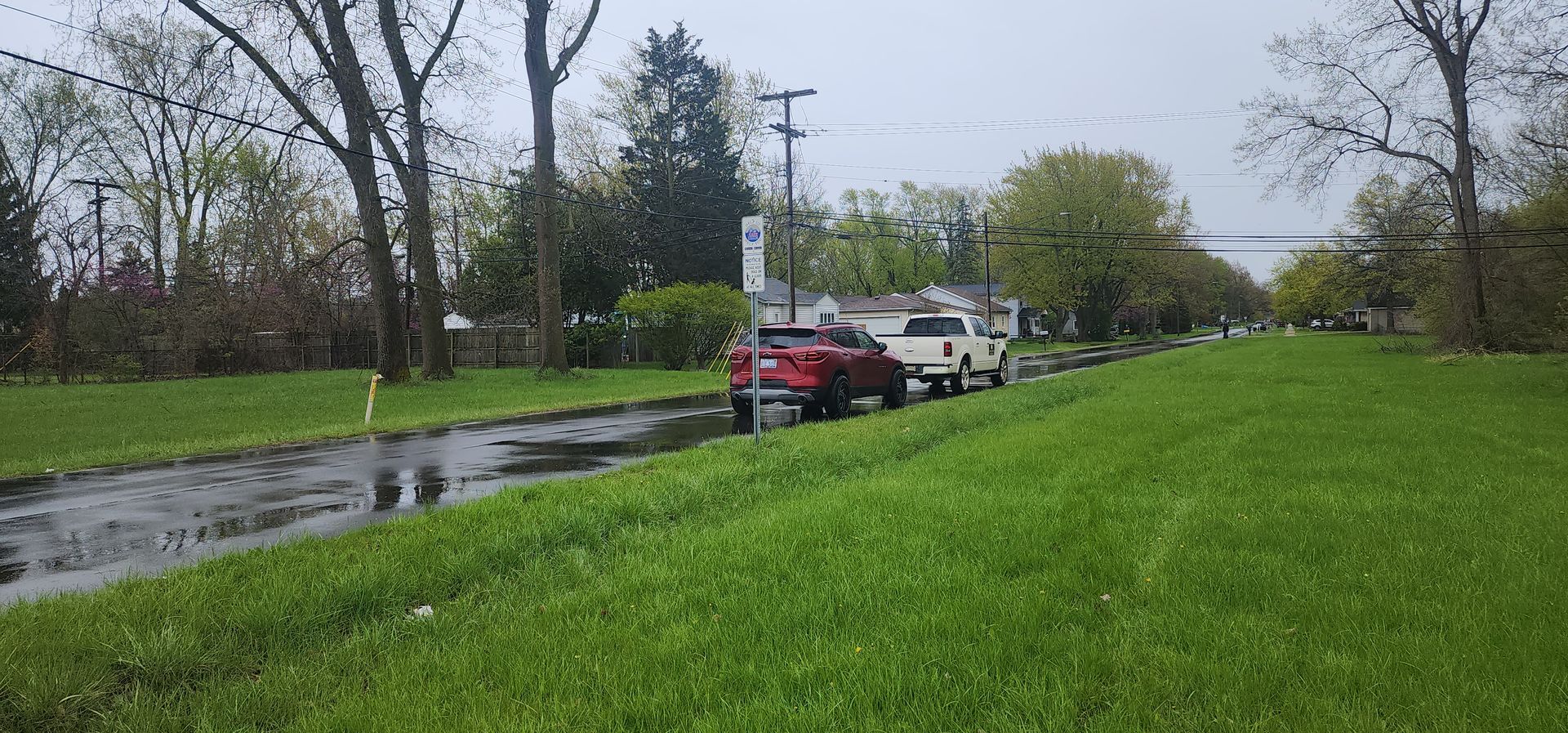 Red SUV pulling a white trailer on a wet road next to a grassy hill. Trees line the road under a cloudy sky.