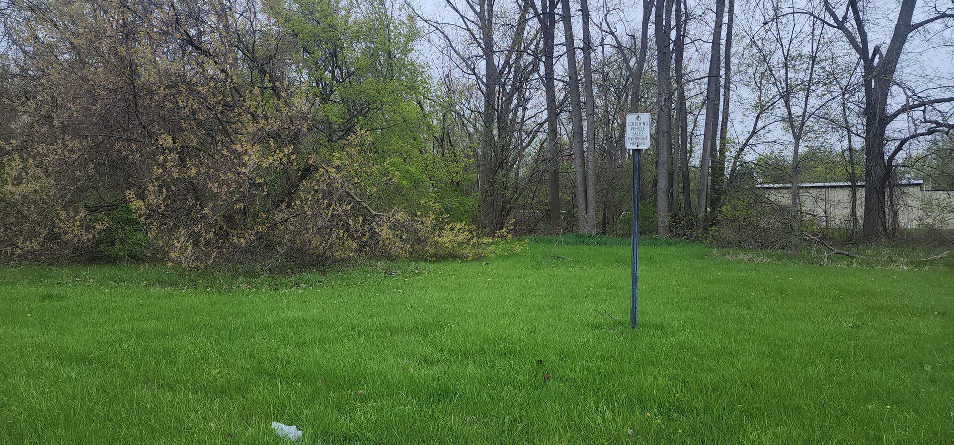 Green lawn with sign in the middle, trees and bushes in the background. Overcast sky.