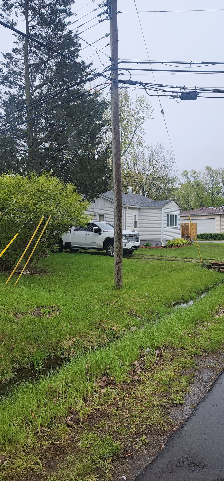 A white pickup truck parked in front of a small white house on a grassy area, telephone pole in the foreground.