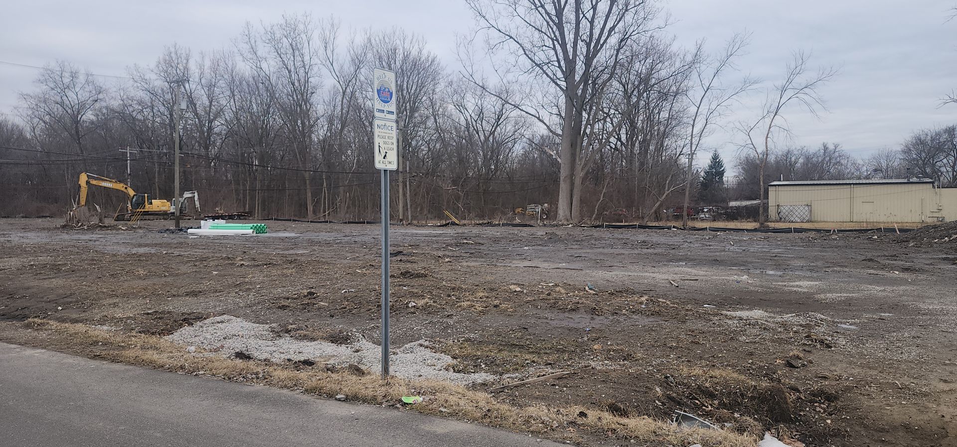 Construction site with exposed earth, trees in background, and a sign.