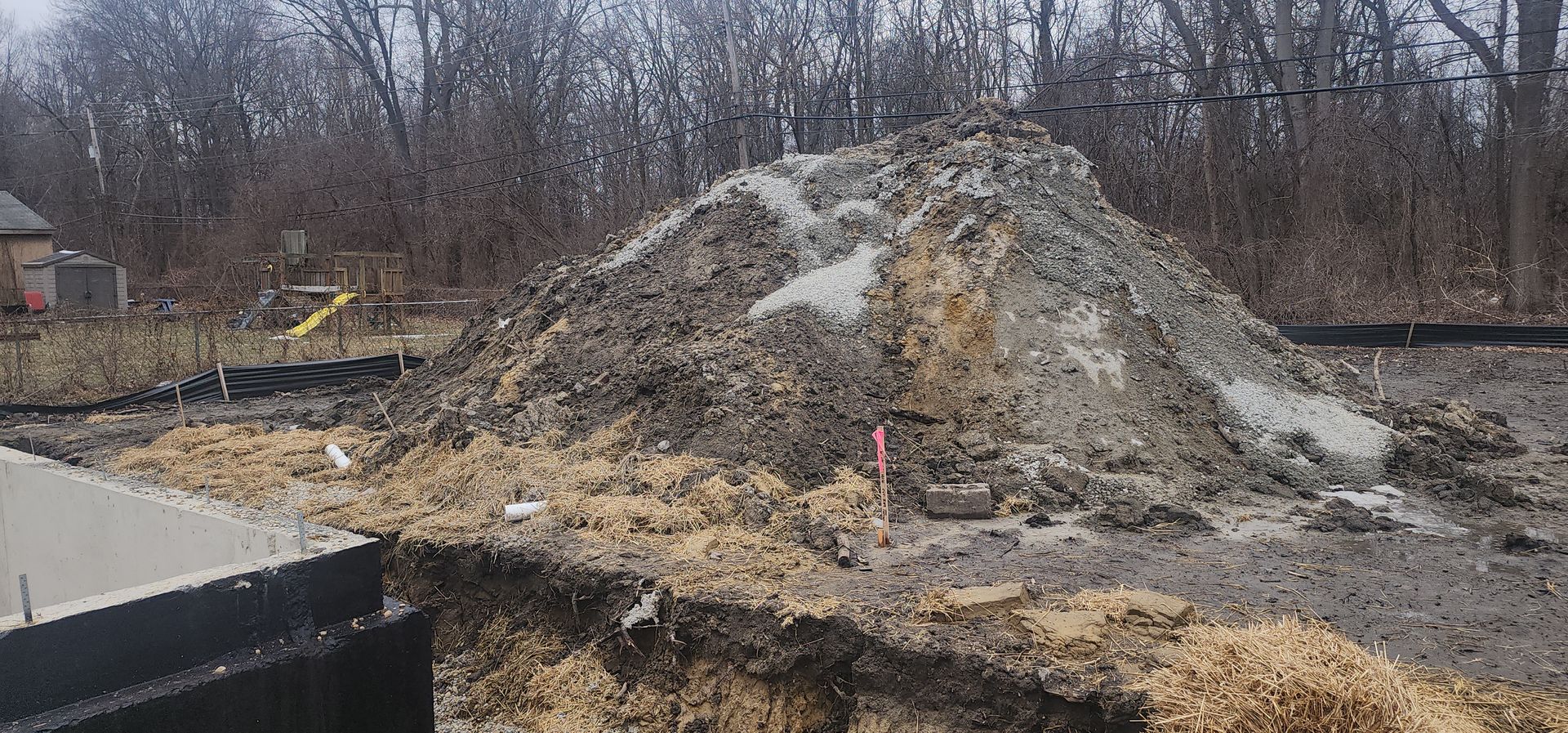 Construction site with a large dirt pile and trees in the background.