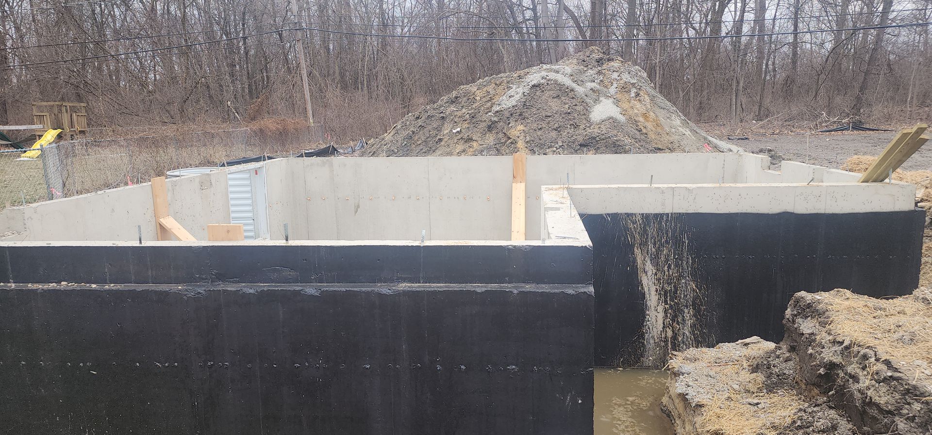 Foundation construction in a dirt lot with a pile of dirt in the background.