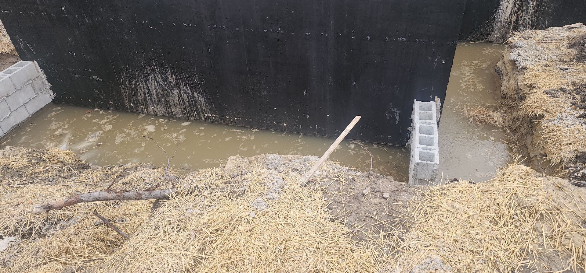 A dark structure with water inside, surrounded by blocks and straw.