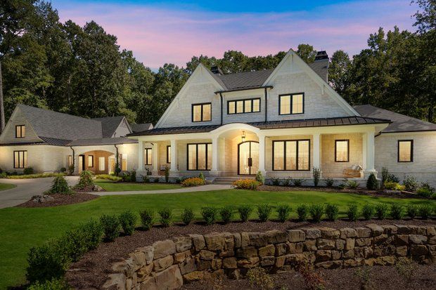 White brick house with black-trimmed windows, arched doorway, lush green lawn, and stone wall.