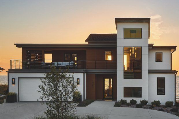 Modern two-story home with white exterior and brown accents at sunset, overlooking water.