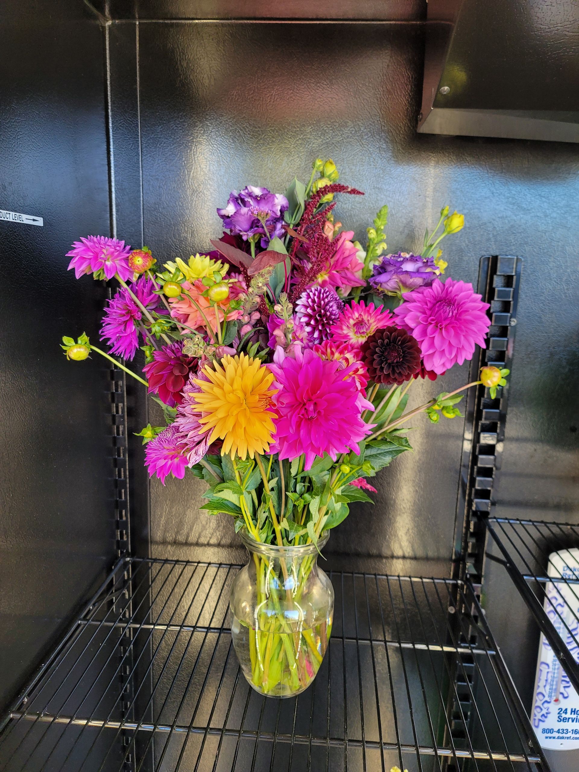 Colorful bouquet of dahlias and other flowers in a clear vase, on a black shelf.