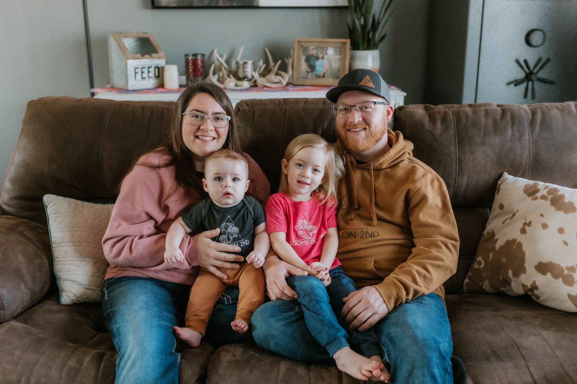 Family of four smiling on brown couch, indoors.