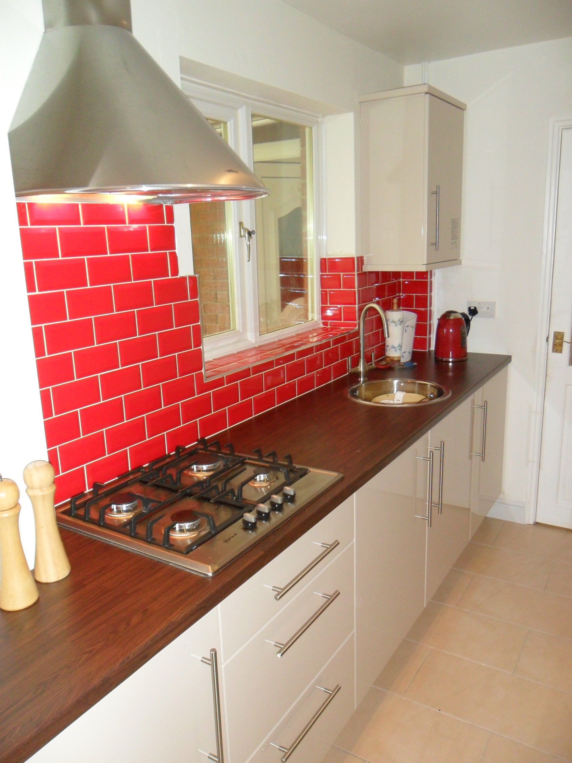 new kitchen bright red wall tiles gloss cream cabinets Axiom worktop cream floor tile hob extractor