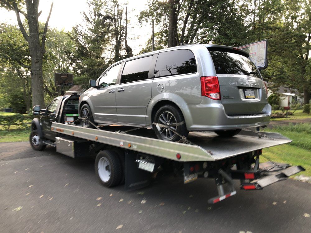 A silver minivan is being towed by a tow truck.