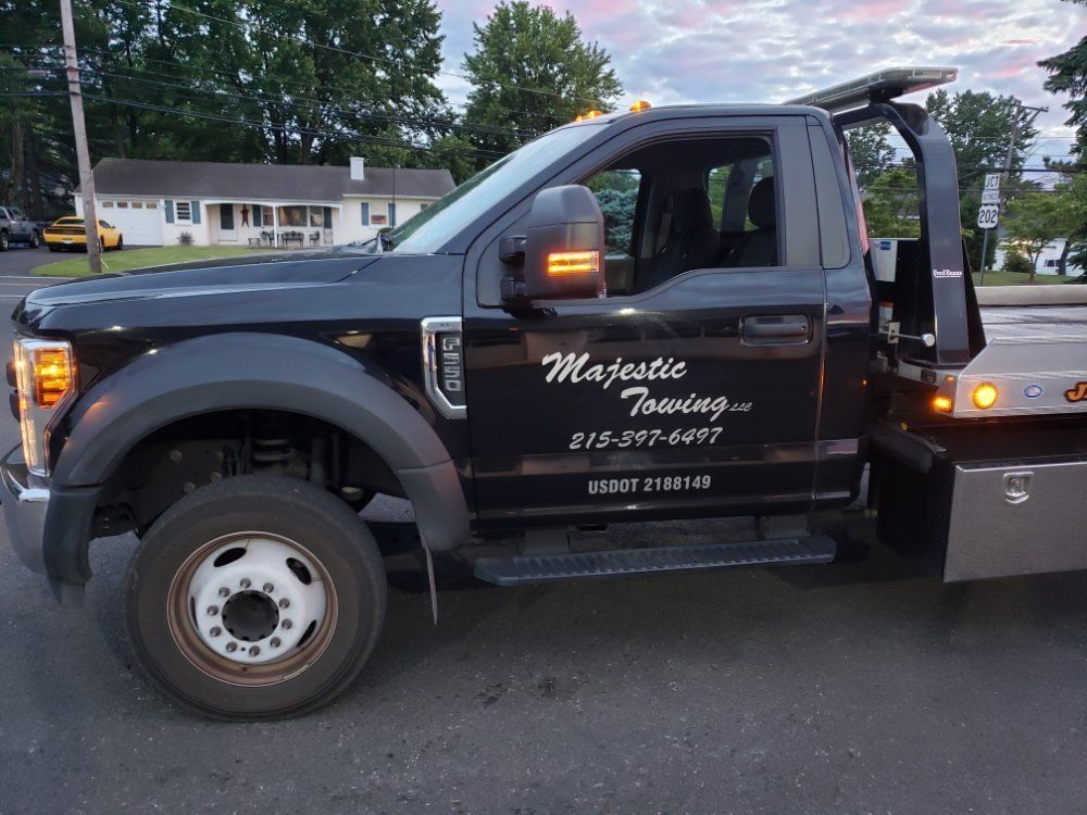 A black tow truck from majestic towing is parked on the side of the road