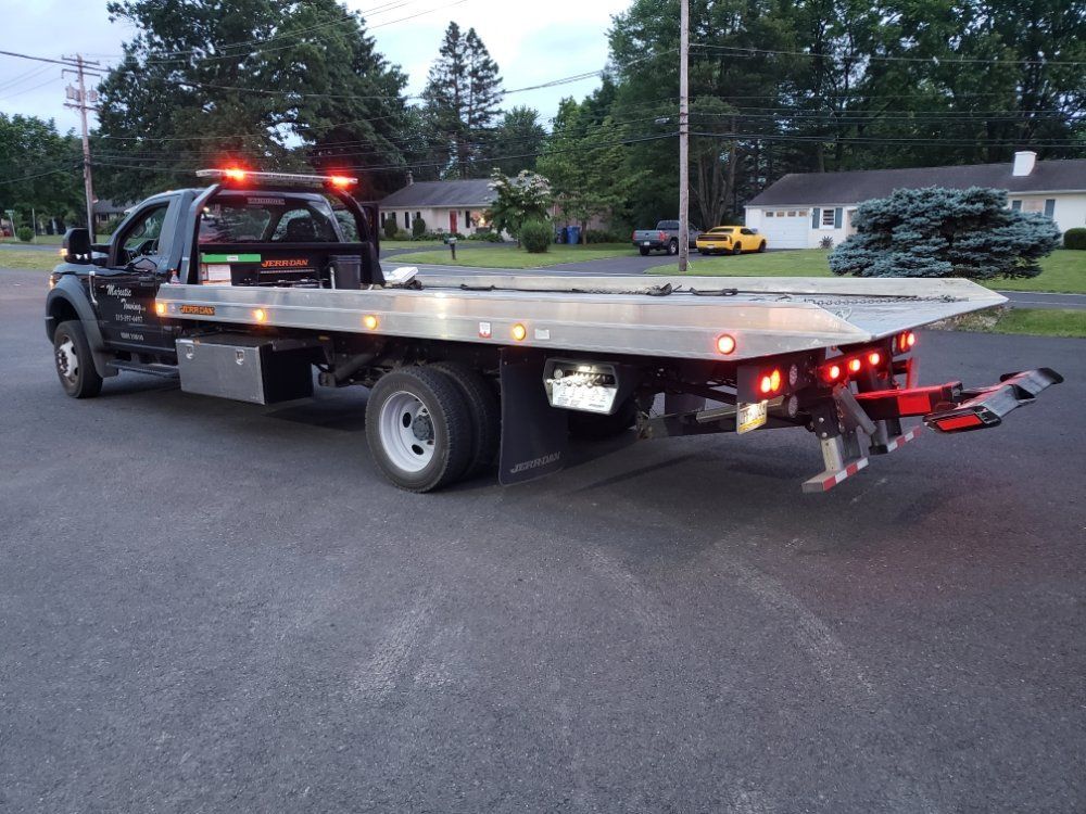 A tow truck with a flat bed is parked on the side of the road